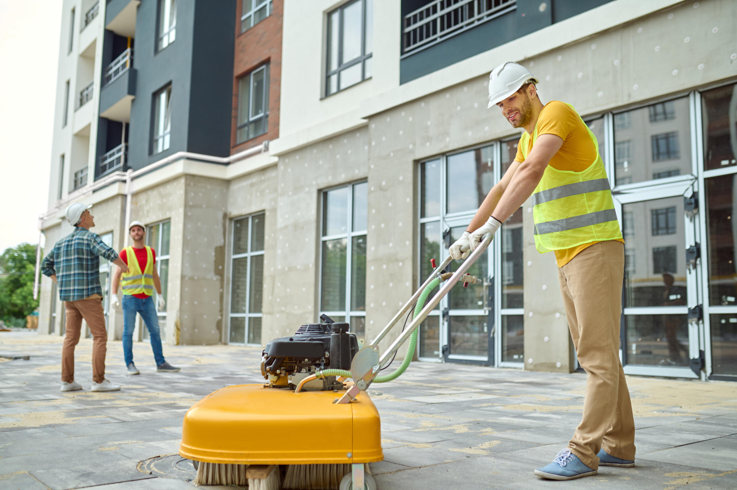 worker cleaning construction site and two men near building